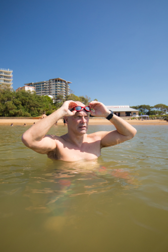 Male open water swimmer wearing goggle standing in water near the shore - Australian Stock Image