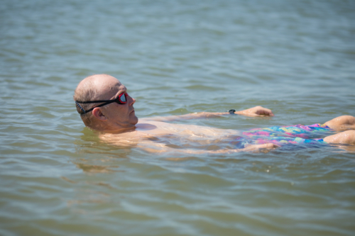 Male open water swimmer wearing goggles float on back in water - Australian Stock Image