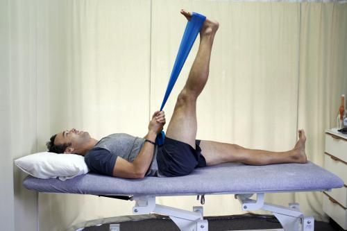 Male patient completing a hamstring stretch on a bed in a physio studio - Australian Stock Image
