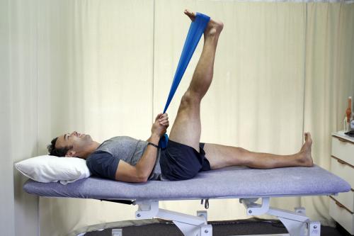 Male patient completing a hamstring stretch on a bed in a physio studio