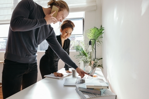 Male professional pointing at a computer screen to show his female colleague - Australian Stock Image