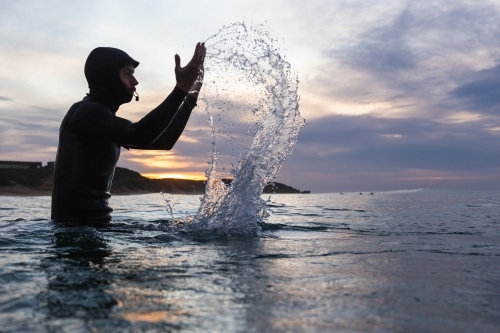 Male surfer splashing in water during sunrise
