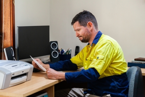 Male tradie in his 30's sitting at his computer stressed out over paperwork