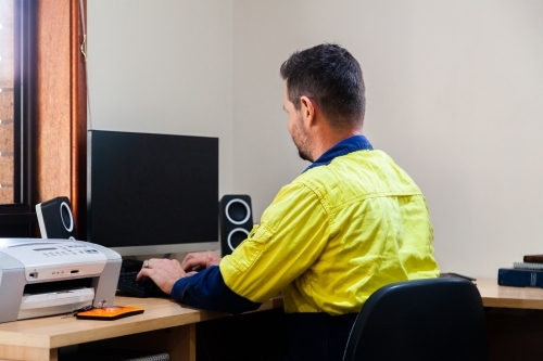 Male tradie using computer in home office - Australian Stock Image