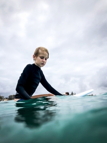 Male youth sitting on boogie board waiting for waves on overcast day