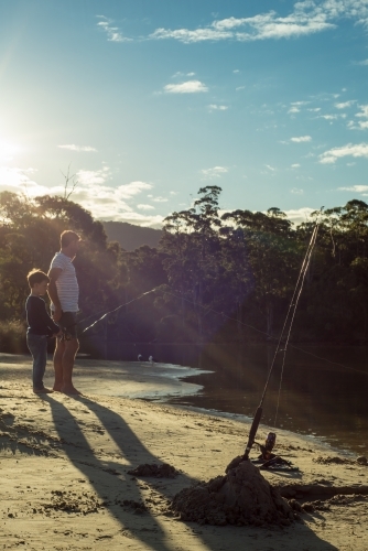 Man and boy fishing at river outlet with sun ray light