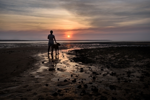 Man and dog on beach at sunset
