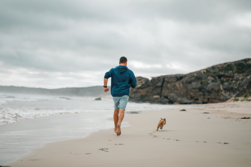 Man and dog running on the beach in Portland, Victoria - Australian Stock Image