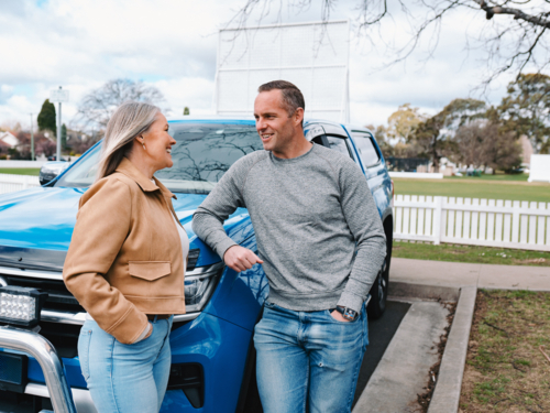 Man and woman having conversation while leaning on blue car parked outdoors - Australian Stock Image