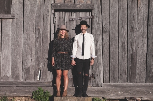 Man and woman holding hands standing against rustic wooden wall - Australian Stock Image