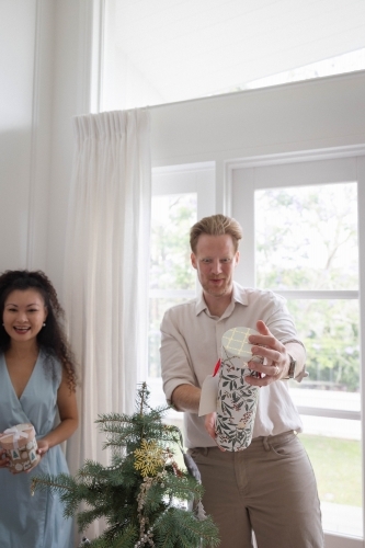 Man and woman holding present next to Christmas tree - Australian Stock Image