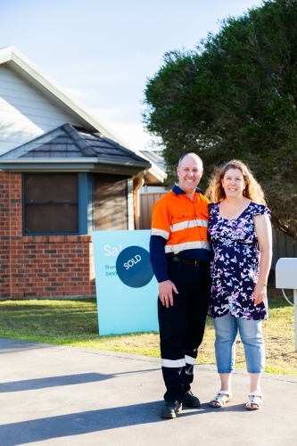 Man and woman in front of investment property house with sold sign - Australian Stock Image