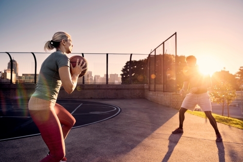 Man and woman passing basketball in sunlight - Australian Stock Image