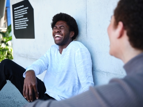 Man and woman sitting against a concrete wall having a conversation - Australian Stock Image