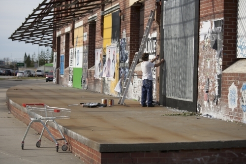 Man applying poster to wall of abandoned warehouse - Australian Stock Image