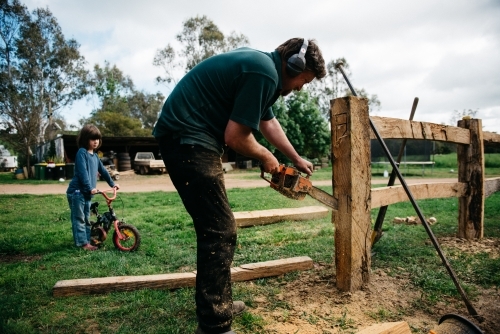 Man building post & rail fence, daughter watching - Australian Stock Image