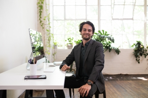 Man facing a camera sitting at a desk in a creative warehouse studio - Australian Stock Image