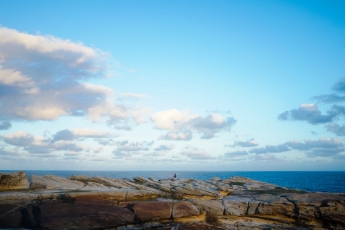 Man fishing alone from a cliff of rocks beside the ocean - Australian Stock Image