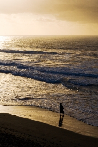 Man fishing on beach at dusk - Australian Stock Image
