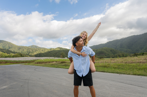 Man gives a woman a piggyback ride on a country road in Queensland - Australian Stock Image