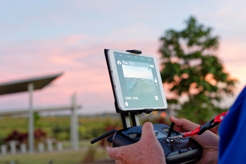 Man holding a controller watching flight path of drone at sunset - Australian Stock Image