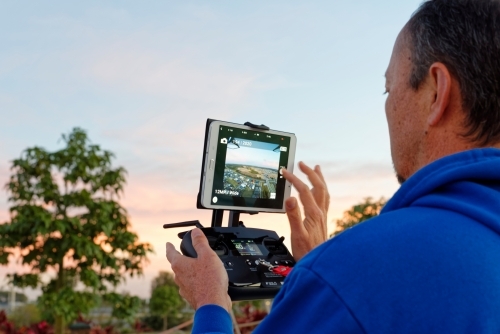Man holding a controller with screen on watching the drone, UAV, RPAs in flight - Australian Stock Image