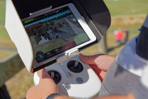 Man holding a white controller with aerial views visible flying his drone, uav, rpas