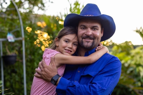 man holding his little girl who is hugging him around the neck - Australian Stock Image