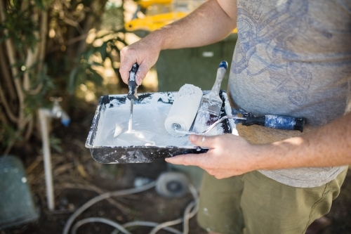 Man holding paint tray with roller and pain brush mixing paint - Australian Stock Image