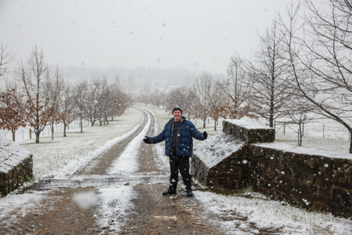 Man in 40s standing with arms out smiling in driveway with snow falling - Australian Stock Image
