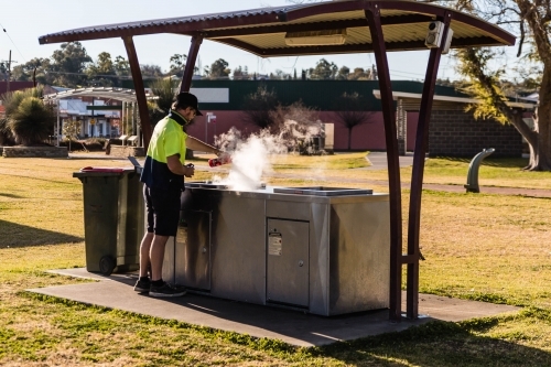 Man in hat cleaning hot barbecue with steam - Australian Stock Image