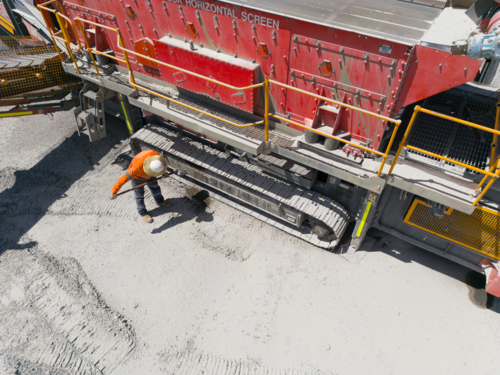 Man in high visibility clothes checking the sides of the crusher. - Australian Stock Image