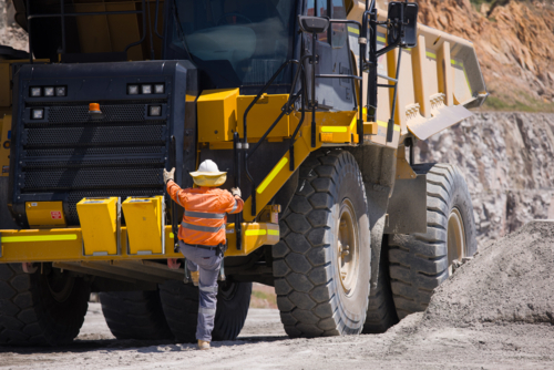 Man in high visibility clothes climbing up the dump truck. - Australian Stock Image
