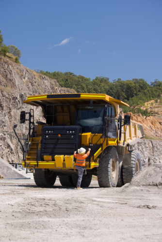 Man in high visibility clothes climbing up the dump truck. - Australian Stock Image