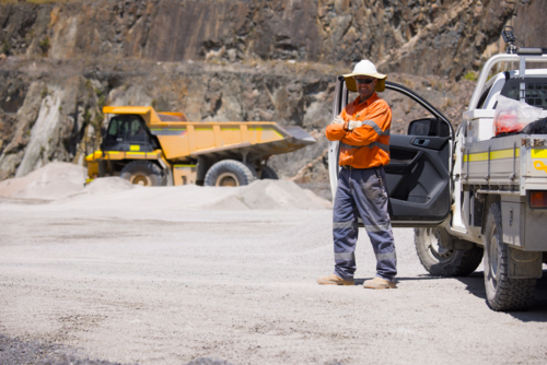 Man in high visibility clothes standing with arms crossed beside ute on mine site - Australian Stock Image