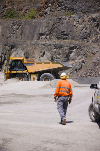 Man in high visibility clothes walking away from his car in open cut mine - Australian Stock Image
