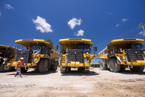 Man in high visibility clothing walking in front of haul trucks. - Australian Stock Image