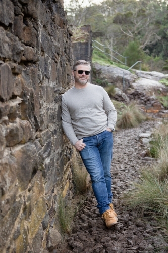Man in his 30's leaning against an historic brick wall - Australian Stock Image