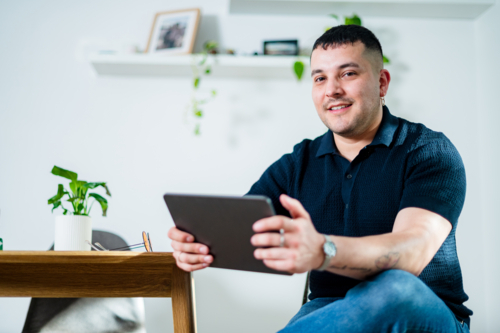 Man in his 30s sits comfortably at home, engaging with a tablet in a relaxed setting. - Australian Stock Image