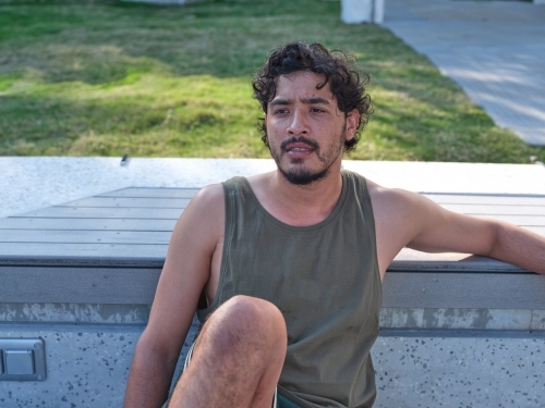 Man in singlet sitting against stair bench - Australian Stock Image