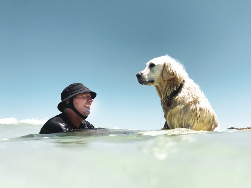 Man in surf hat with Labrador dog in the ocean looking at each other