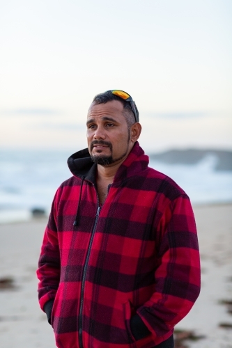 Man in warm checked jacket at beach with sunnies on head - Australian Stock Image