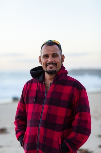 Man in warm checked jacket at beach with sunnies on head