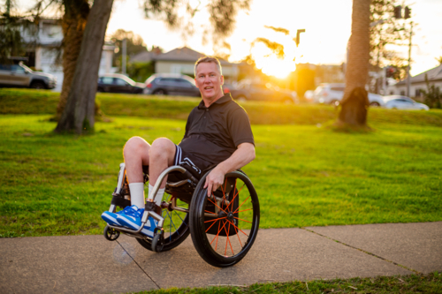 Man in wheelchair smiles while doing tricks on his wheelchair - Australian Stock Image