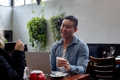 Man talking with friend whilst drinking coffee at cafe - Australian Stock Image
