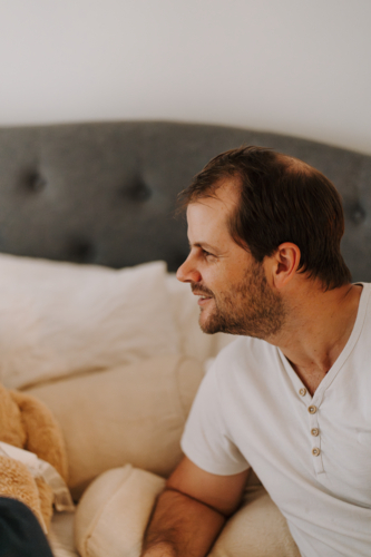 Man leaning on bed looking off-camera - Australian Stock Image