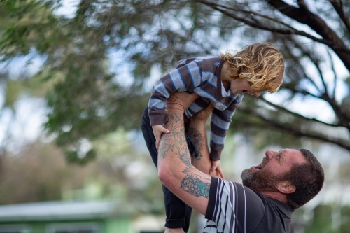 Man lifting young child in the air outside - Australian Stock Image