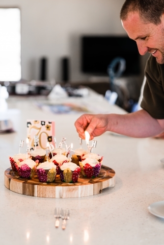 man lighting candles on cupcakes for birthday party - Australian Stock Image