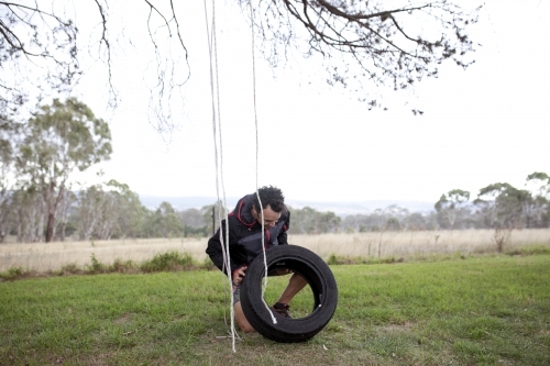 Man making a tyre swing in country backyard - Australian Stock Image