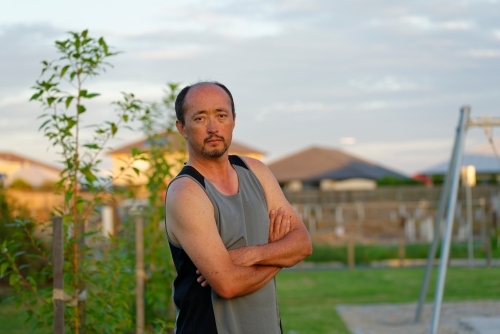 Man of mixed race standing with folded arms at sunset in a park - Australian Stock Image